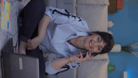 Vertical-video-of-Home-office-worker-woman-talking-on-the-phone-happily.
